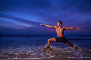 Man in yoga warrior pose on ocean beach at dusk